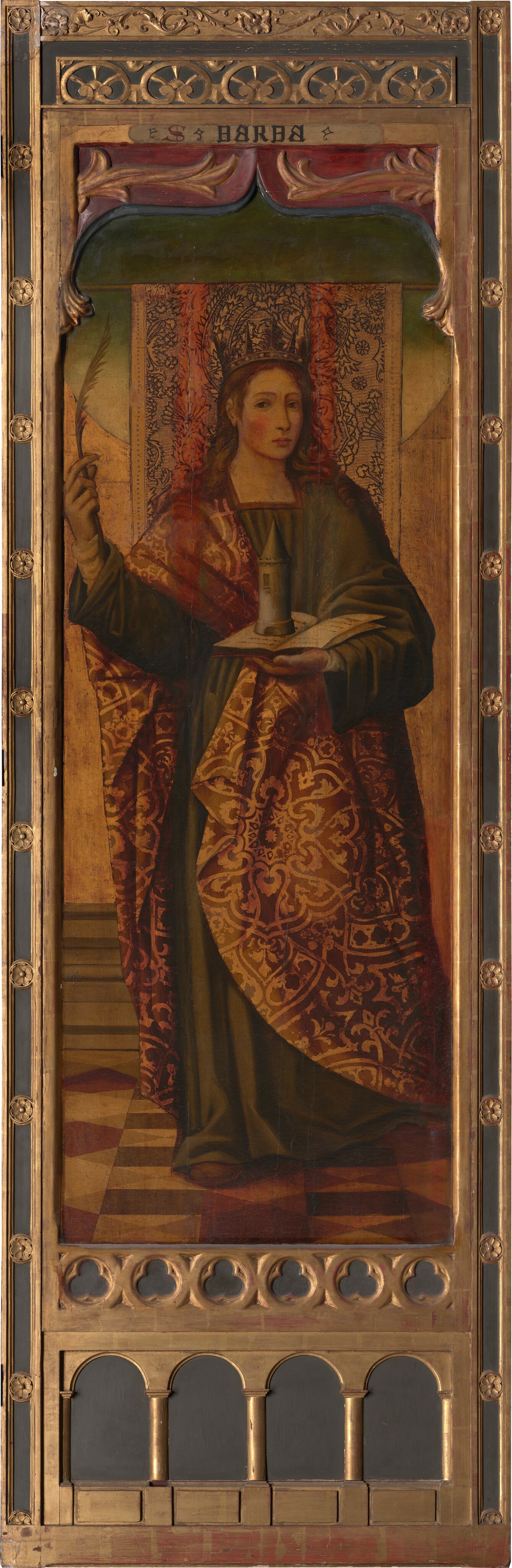 This image shows a woman standing upright, facing the viewer. She has long wavy hair and is dressed in a robe with intricate patterns in red and gold over a green garment. She wears a golden crown and holds a white feather in her right hand and supports a small tower on an open book in her left hand. The background features ornamental design and the painting is in a decorative wooden frame. Above her head is an inscription that reads "SANTA BARBA."