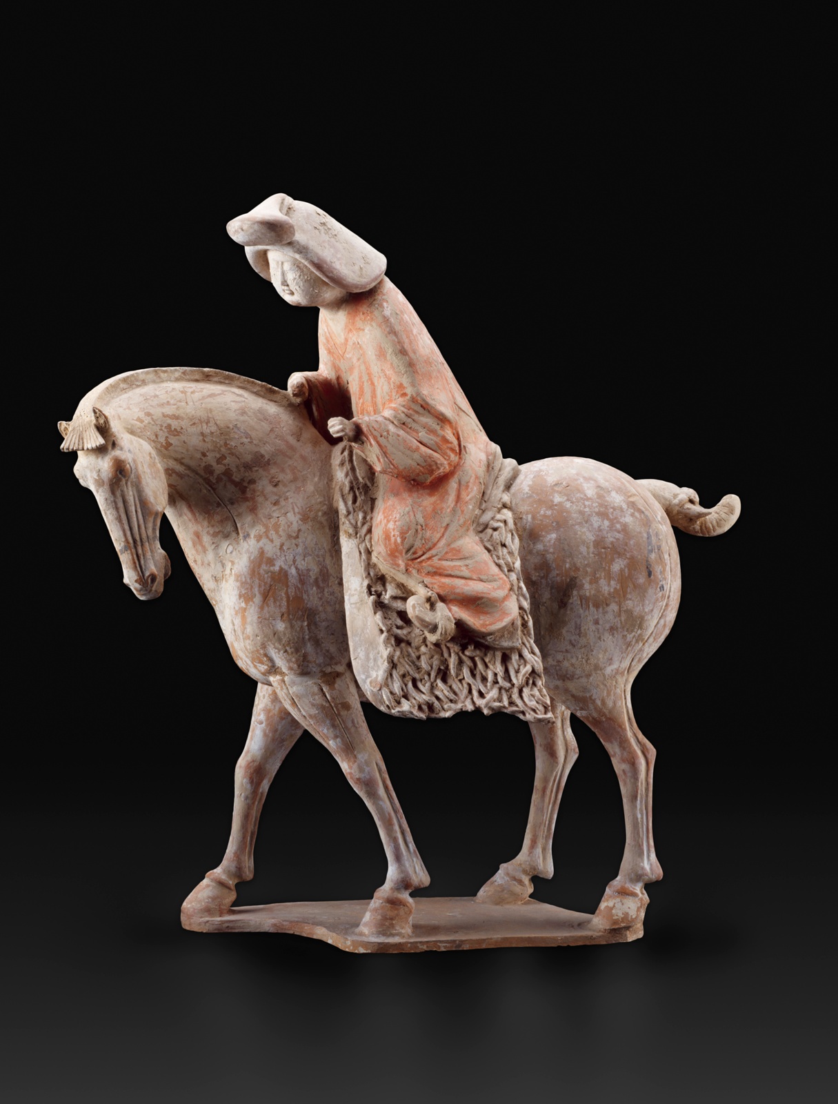 A female figure with a round face in a full orange robe is bent almost wearily as she rides a horse. White pigment has worn away on the horse, and orange has worn from her robe, revealing a terracotta tone.