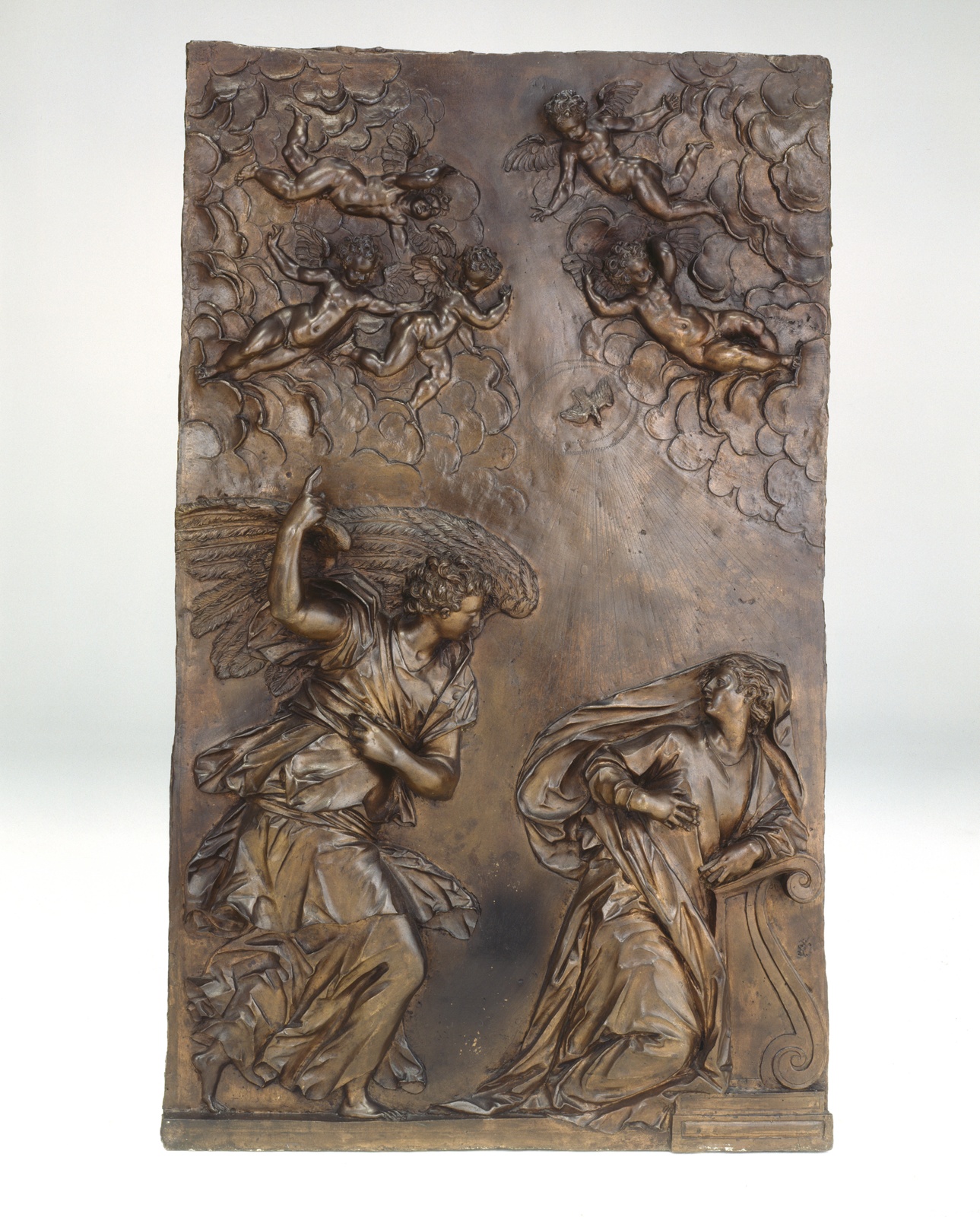 Relief sculpture of angel confronting Virgin Mary. Cherubs and dove in sky.
