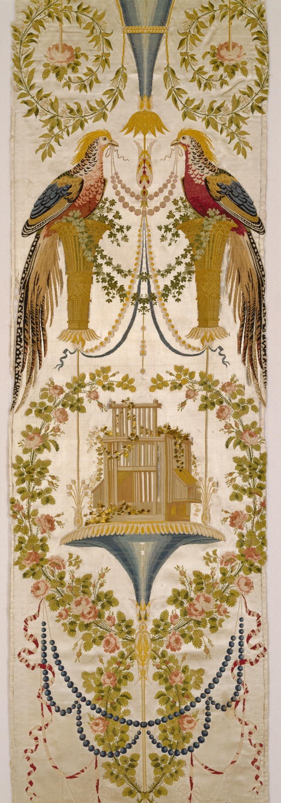 A textile featuring two pheasants in the upper portion facing one another, strands of golden beads held between them in their beaks, symmetrical garlands above and below them, a golden structure near the middle, and curled ribbons embroidered near the bottom.