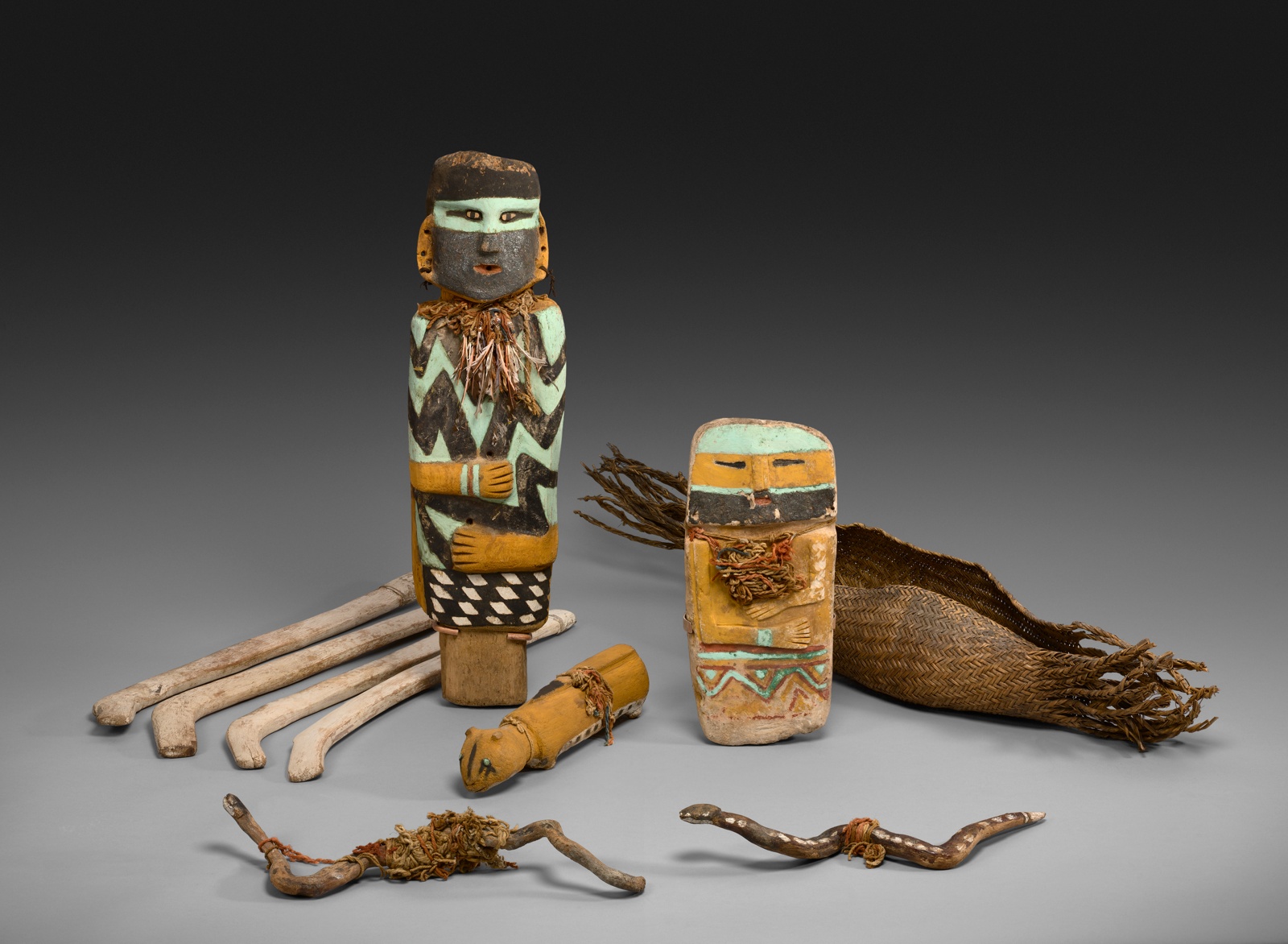 Carved ceremonial objects colored with orange and blue of a man, woman, snake, curved sticks, and cougar.