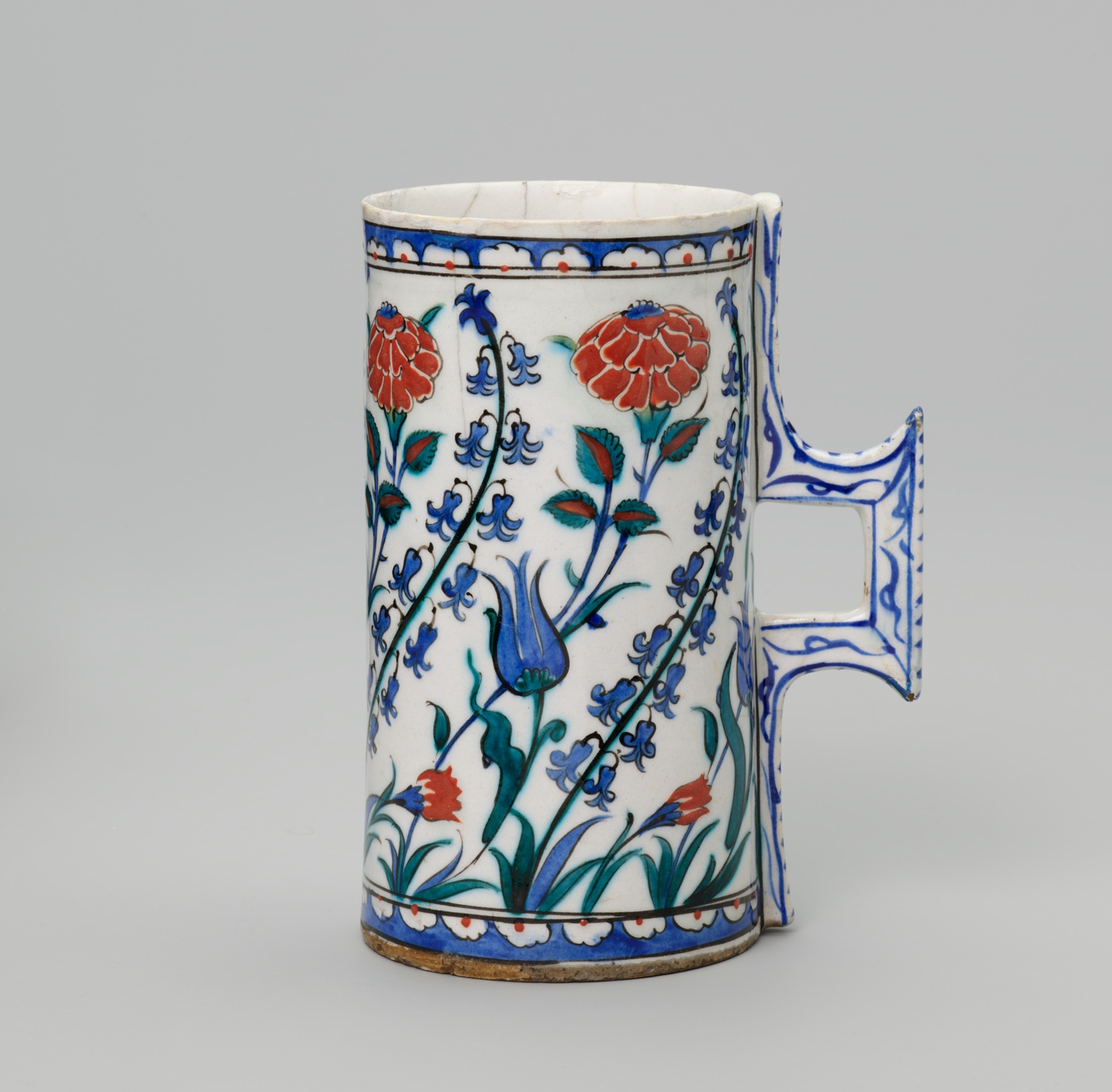 White ceramic cup with red and blue flowers and square handle.