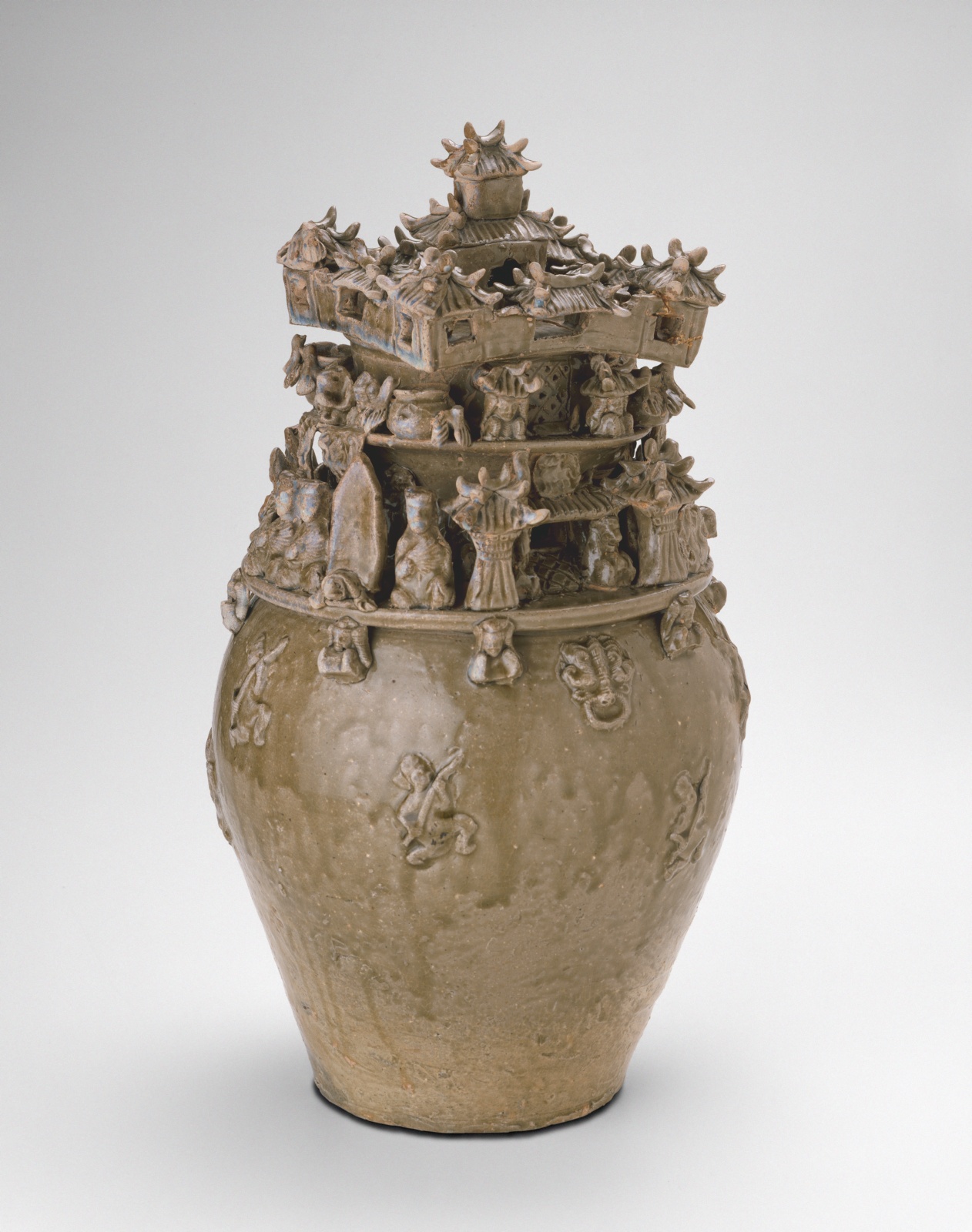 Medium sized olive colored urn, upper half carved into figures and structures.