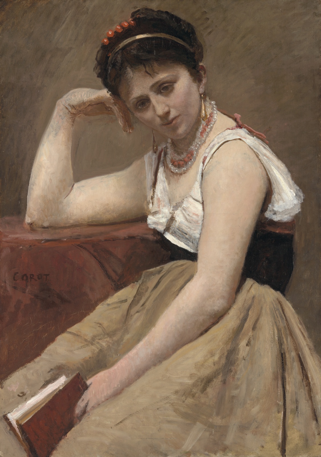 A  pensive faced woman sits, slightly hunched, holding a book.