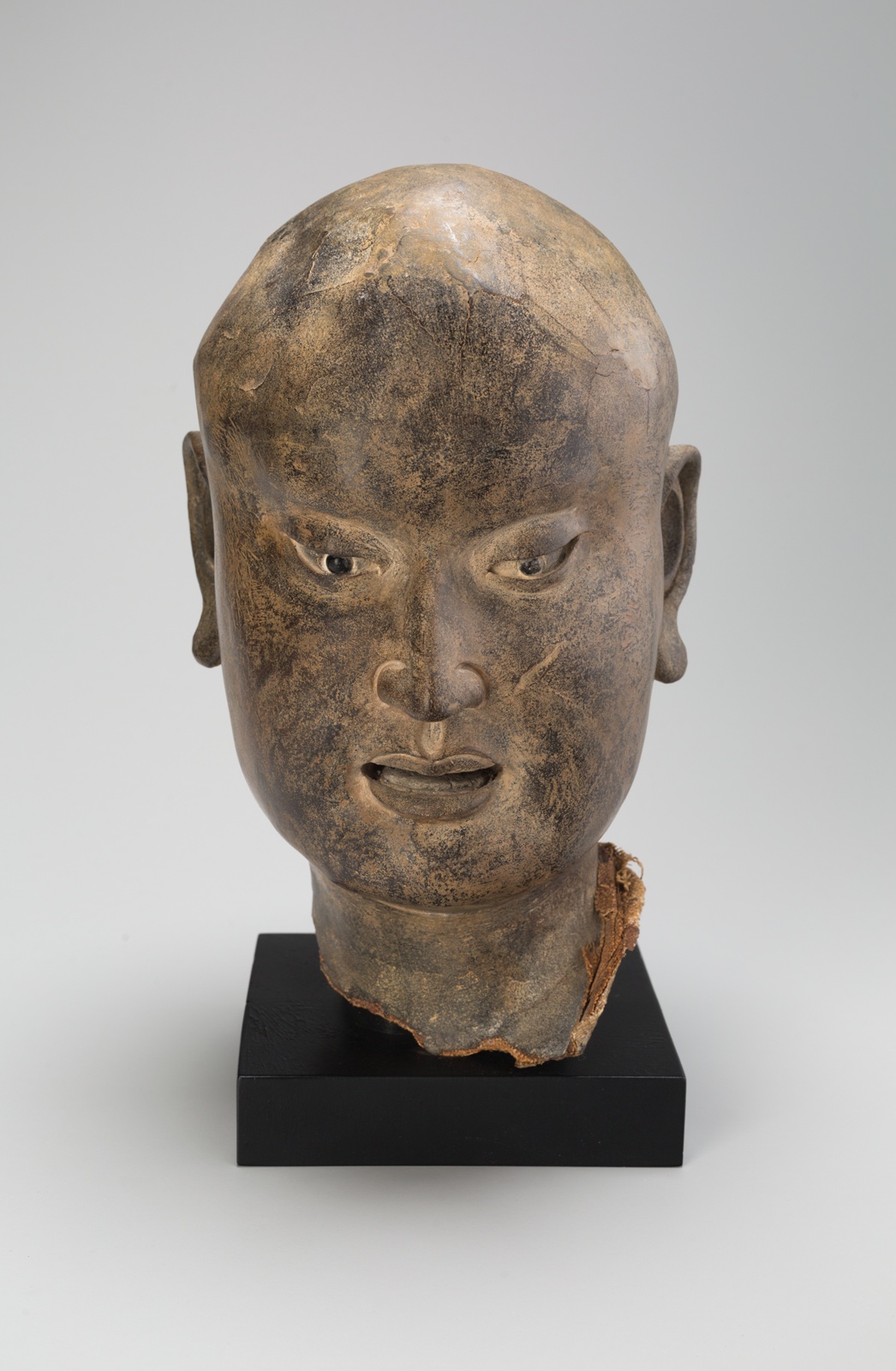 Sculpture of Asian man’s head, he is bald with detailed angular facial features.