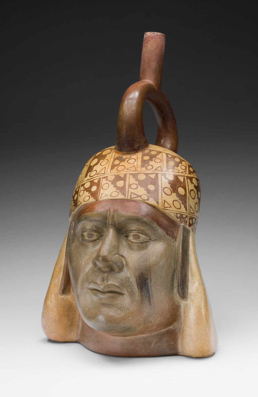 Sculpted head of a medium-skinned man in a beige headdress with geometric pattern and distinctive stirrup-shaped top piece.