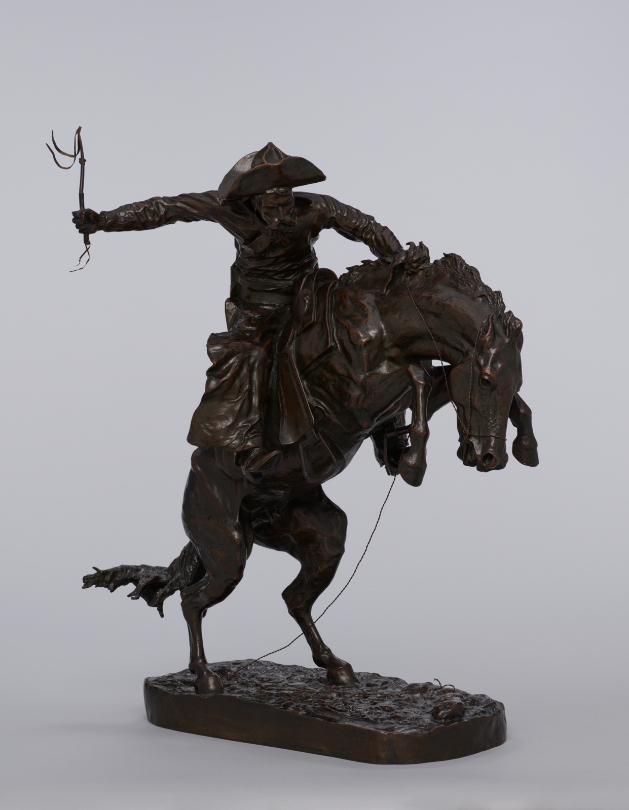 Brown bronze statue of man with riding crop atop a rearing horse.